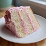 A perfect slice of Strawberry Whipped Cream Cake showing layers of white cake and pink frosting.