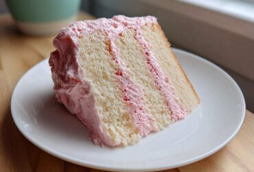 A perfect slice of Strawberry Whipped Cream Cake showing layers of white cake and pink frosting.
