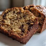 A close-up view of two slices of moist vegan banana bread studded with chocolate chips on a white plate.