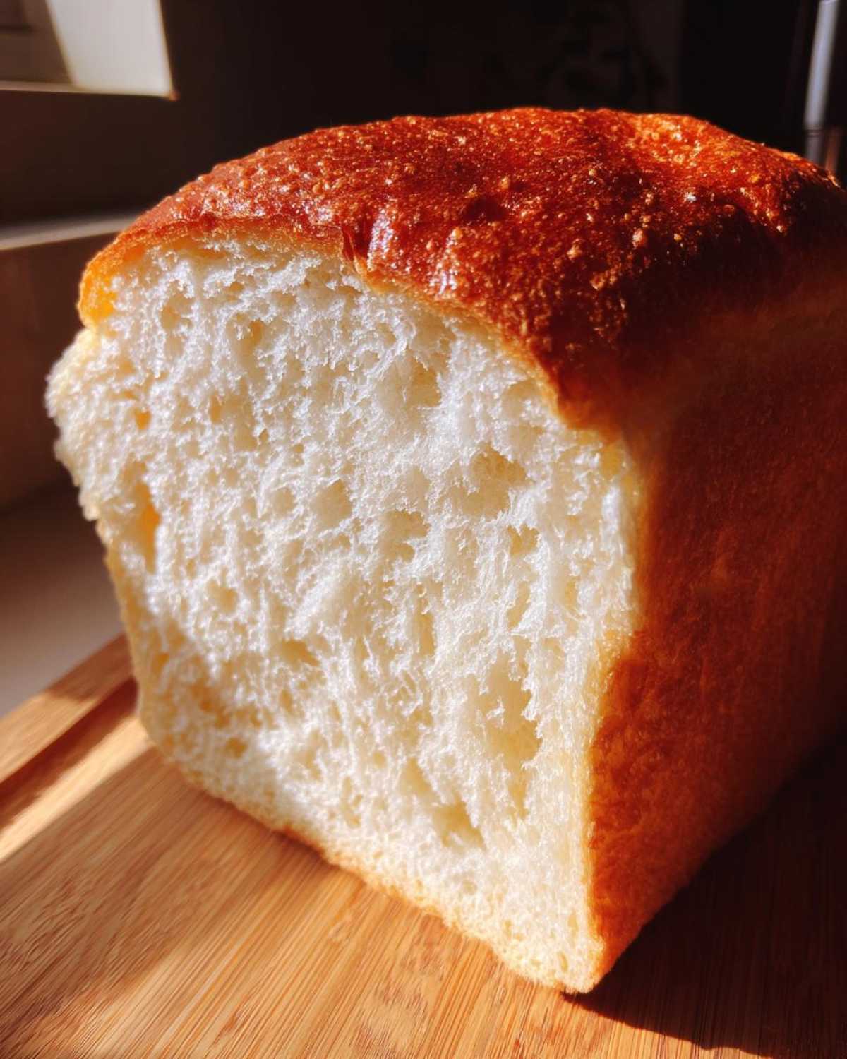 A close-up view showing the incredibly soft, white crumb texture of a freshly baked japanese milk bread loaf with a golden brown, shiny crust.