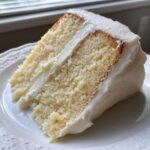 Close-up of a moist slice of vanilla cake recipe layered with thick white buttercream frosting.