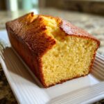 A close-up of a golden-brown loaf of sourdough cornbread, showing its moist, yellow crumb texture.