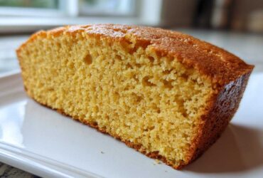 Close-up view of a thick slice of golden sourdough cornbread showing its moist, crumbly texture.