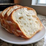 Three thick slices of homemade sourdough sandwich bread showing a soft, open crumb texture on a white plate.