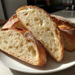 Slices of freshly baked sourdough sandwich bread showing an open, airy crumb structure on a white plate.