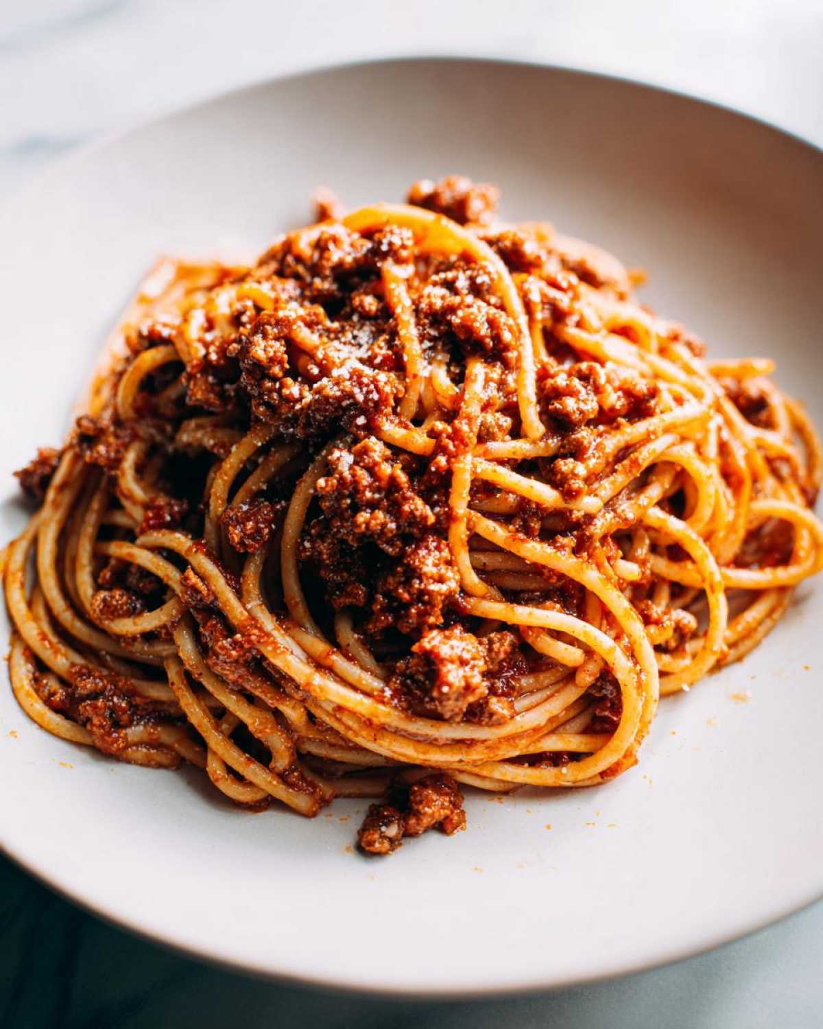Close-up of spaghetti generously coated in rich, meaty bolognese sauce and topped with grated cheese.