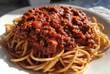 Close-up of spaghetti topped generously with rich, meaty bolognese sauce on a white plate.