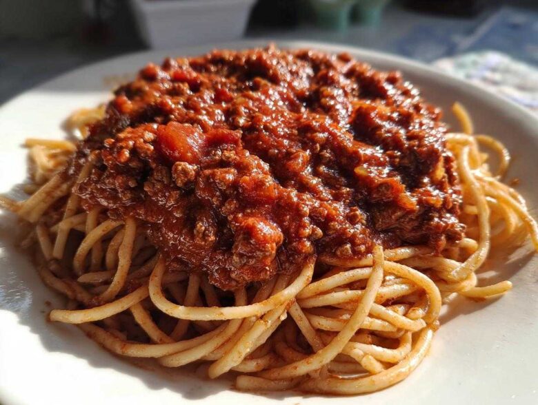 Close-up of spaghetti topped generously with rich, meaty bolognese sauce on a white plate.