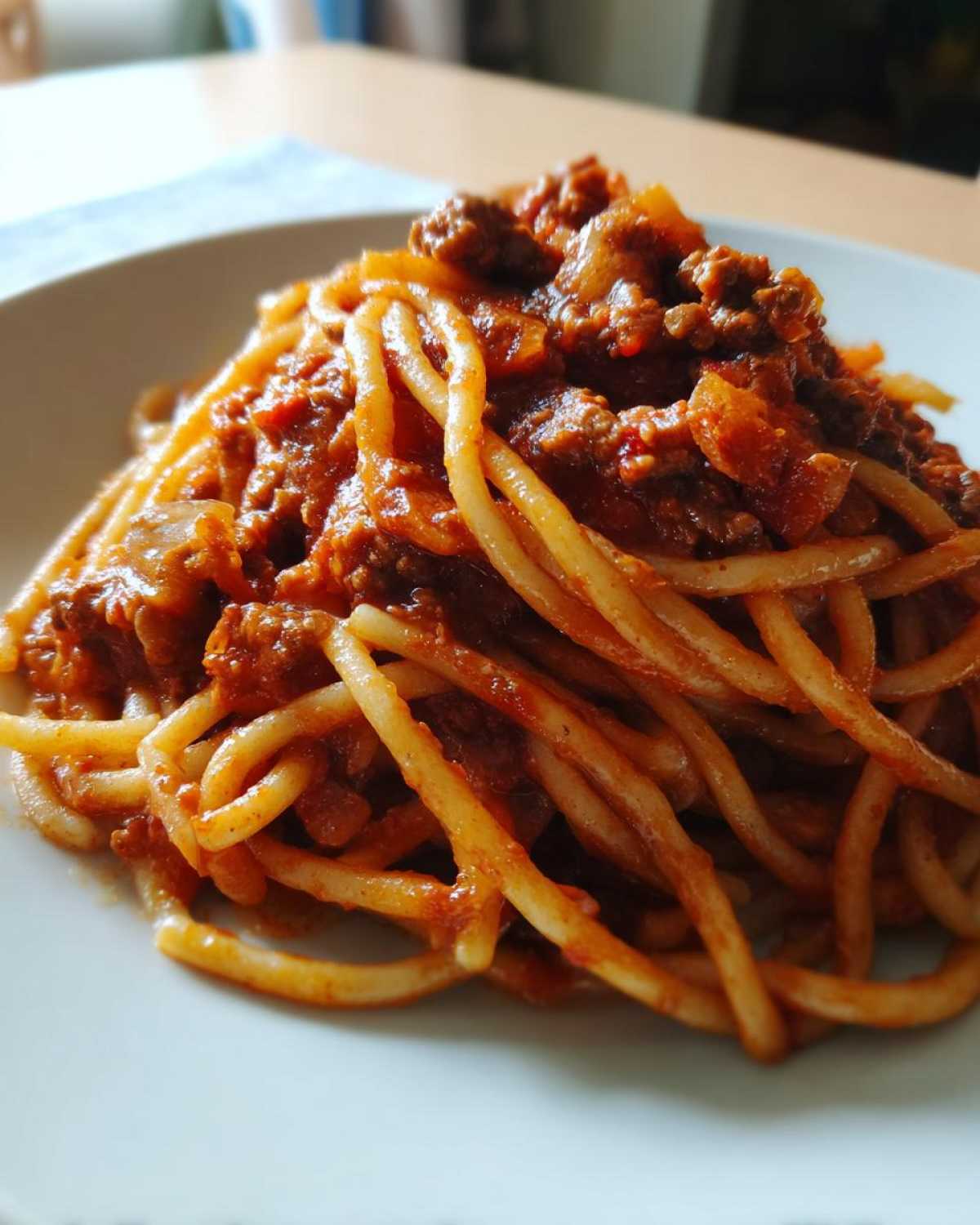 Close-up of spaghetti noodles generously coated in rich, meaty bolognese sauce served on a white plate.