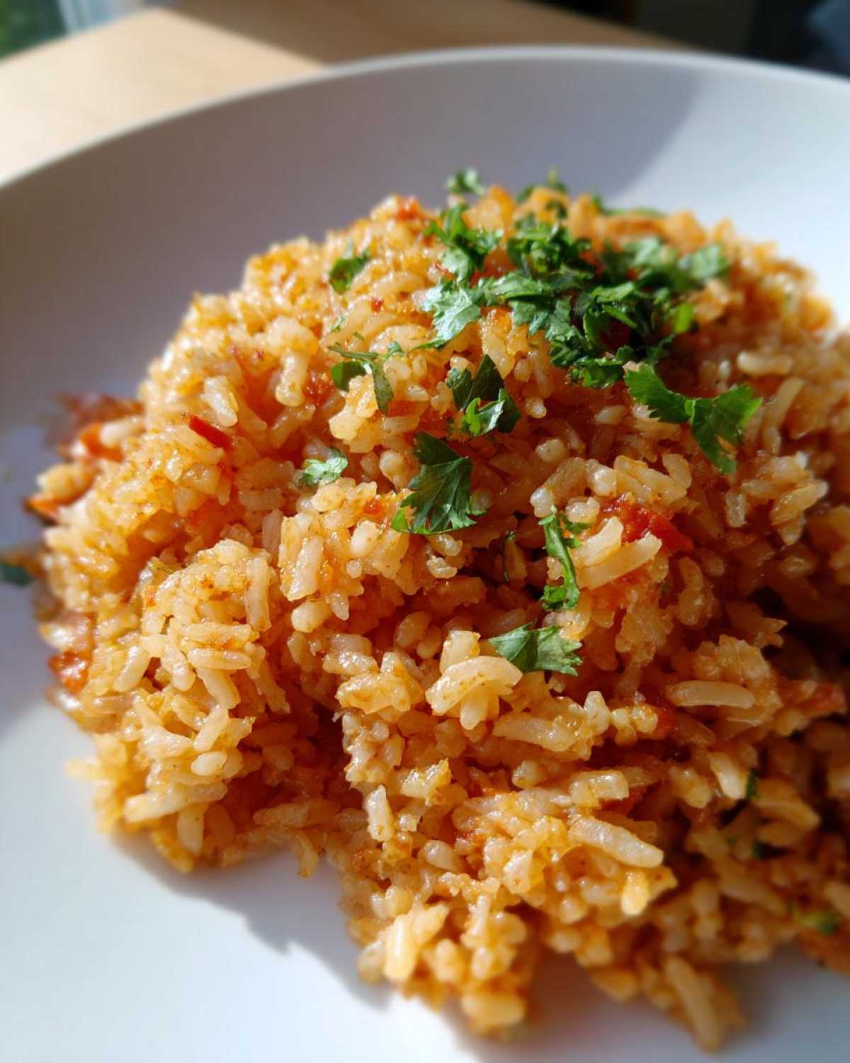 Close-up of fluffy, orange-hued Spanish rice topped with fresh chopped cilantro on a white plate.