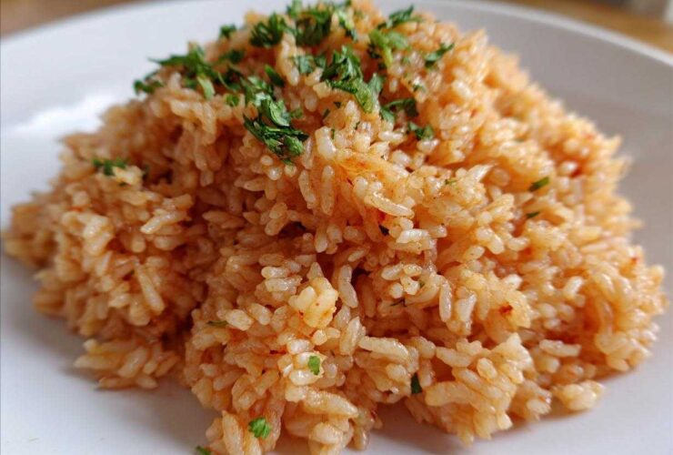 Close-up of a mound of perfectly cooked, reddish-orange Spanish rice garnished with fresh chopped parsley on a white plate.