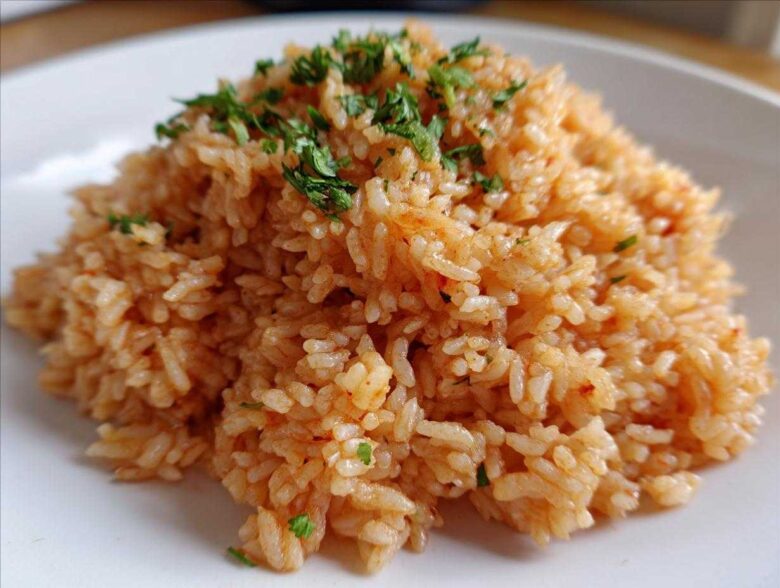 Close-up of a mound of perfectly cooked, reddish-orange Spanish rice garnished with fresh chopped parsley on a white plate.