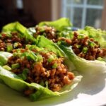 Close-up of three fresh chicken lettuce wraps filled with savory ground chicken and topped with bright green scallions.