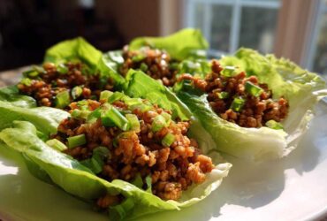 Close-up of three fresh chicken lettuce wraps filled with savory ground chicken and topped with bright green scallions.