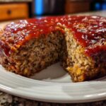Close-up of a round stove top stuffing meatloaf with a slice removed, covered in a shiny red glaze.