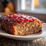 A close-up of a freshly baked stove top stuffing meatloaf topped generously with a bright red ketchup glaze.