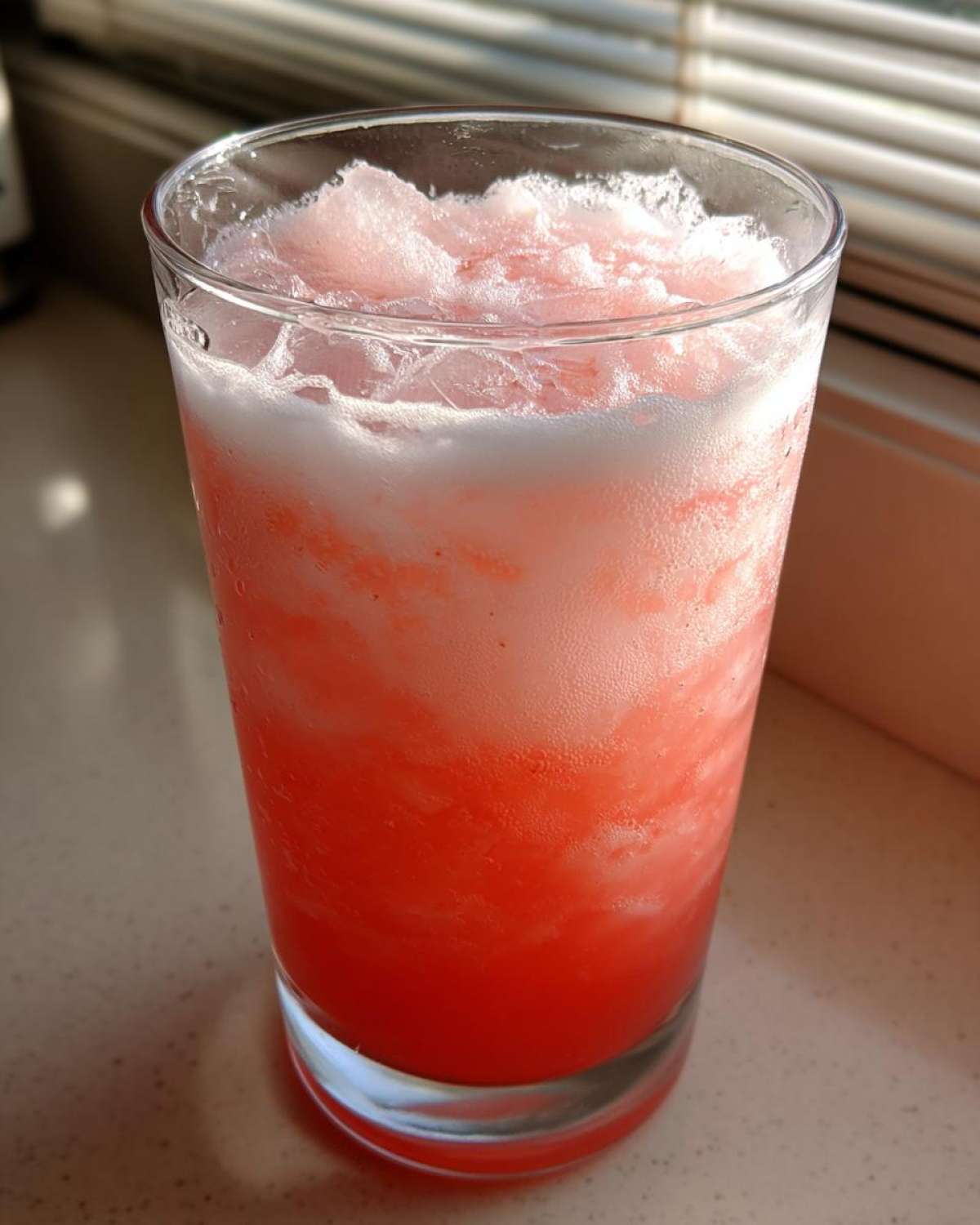 A tall glass filled with bright pink, icy Irresistible Strawberry Piña Colada Punch topped with frothy ice.