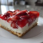 A close-up of a square slice of strawberry pretzel salad showing the pretzel crust, cream cheese layer, and strawberry gelatin topping.