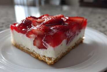 A close-up of a square slice of strawberry pretzel salad showing the pretzel crust, cream cheese layer, and strawberry gelatin topping.