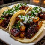 A close-up of several homemade Tacos al pastor served on corn tortillas, topped with marinated pork, pineapple, diced onion, and cilantro.