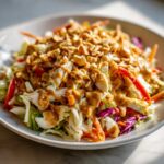 A vibrant bowl of thai chicken salad featuring shredded chicken, crisp vegetables, peanut dressing, and chopped peanuts.