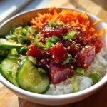 A vibrant close-up of a Tuna Poke Bowl featuring marinated tuna, rice, cucumbers, shredded carrots, and green onions.