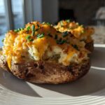 A close-up of a delicious twice baked potato, loaded with creamy filling, melted cheddar cheese, and fresh chives.