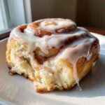 A close-up of one Ultimate Cinnamon Rolls with Creamy Glaze, dripping with thick white icing on a white plate.
