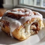 A close-up of one Ultimate Cinnamon Rolls with Creamy Glaze, featuring thick white icing dripping down the side.