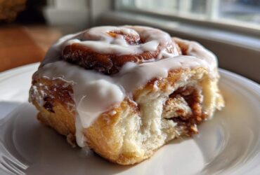 A close-up of one Ultimate Cinnamon Rolls with Creamy Glaze, featuring thick white icing dripping down the side.