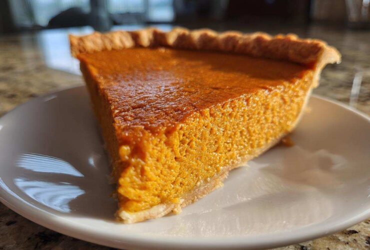 A close-up, sunlit slice of rich orange sweet potato pie resting on a white plate.