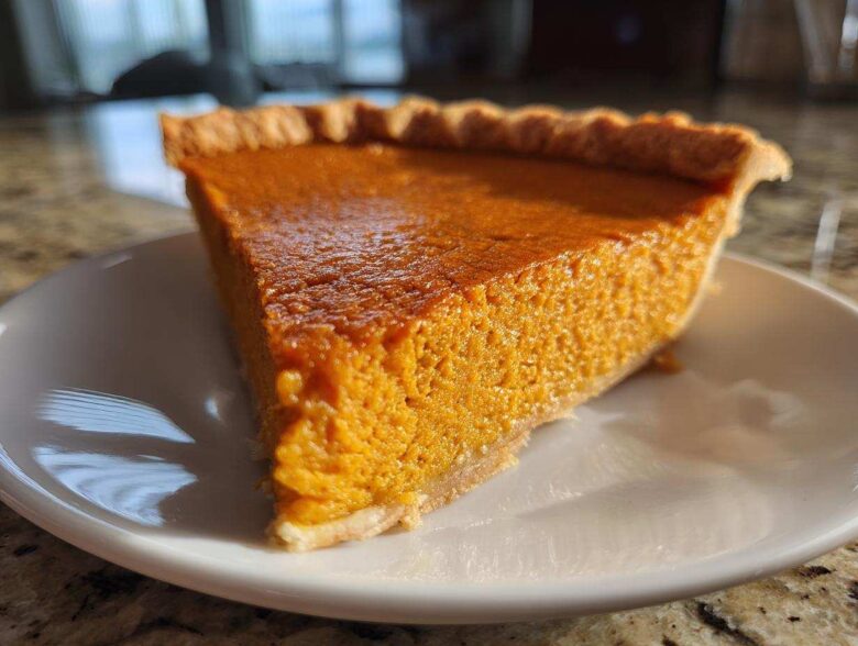 A close-up, sunlit slice of rich orange sweet potato pie resting on a white plate.
