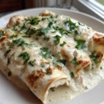 Close-up of three delicious white chicken enchiladas smothered in creamy sauce and topped with fresh parsley.