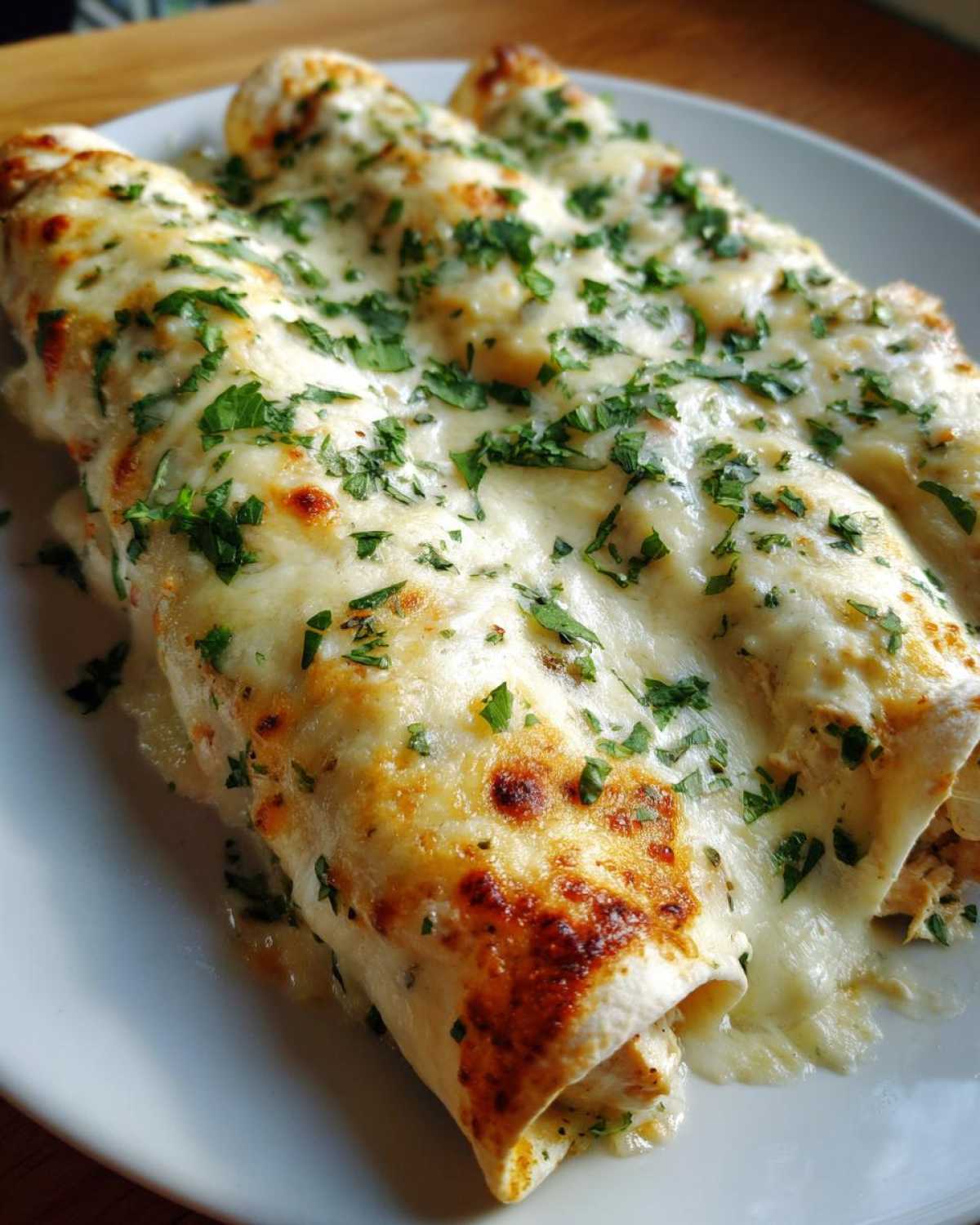 Close-up of three delicious white chicken enchiladas smothered in melted cheese and fresh parsley.