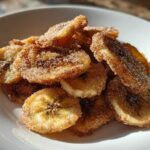 A close-up of crispy Air Fryer Cinnamon Sugar Banana Chips piled high on a white plate, glistening with sugar.
