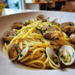 A close-up, appetizing shot of a bowl of Linguine and Clams tossed in a light sauce and garnished with parsley.