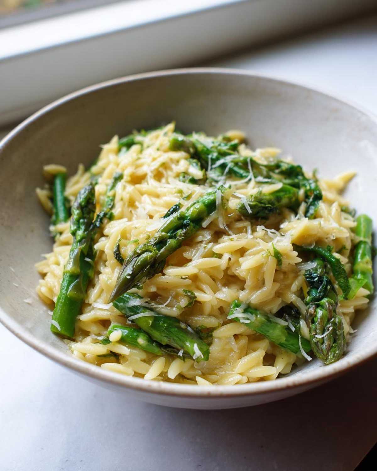 A close-up shot of creamy Asparagus Orzo pasta topped with fresh asparagus spears and grated Parmesan cheese.