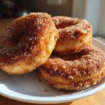 Three freshly Baked Cinnamon Sugar Donuts generously coated in sparkling cinnamon sugar, stacked on a white plate.