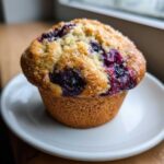 A close-up of a single, perfectly baked Moist and Fluffy Bakery-Style Blueberry Muffin topped with coarse sugar.