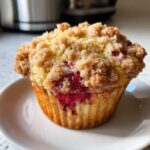 Close-up of a bakery-style Raspberry Streusel Muffins showing a golden crumb topping and burst raspberries.