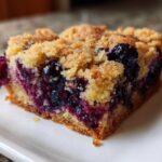 A close-up shot of a single square of rich Blueberry Blondies with a crumbly topping, showcasing the moist interior and bursts of purple blueberries.