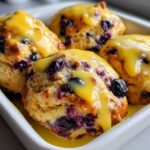 Four golden-brown Blueberry Butter Swim Biscuits generously topped with bright yellow lemon glaze.