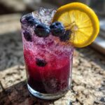 Close-up of a vibrant Blueberry Lemonade with ice, fresh blueberries, and a lemon slice garnish.