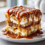 A tall slice of Caramel Apple Cheesecake Cake layered with cream, apples, and drenched in thick caramel sauce.