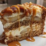 A decadent slice of Caramel Apple Cheesecake Cake layered with cake, cream cheese filling, and apples, topped with caramel sauce.