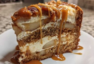 A decadent slice of Caramel Apple Cheesecake Cake layered with cake, cream cheese filling, and apples, topped with caramel sauce.