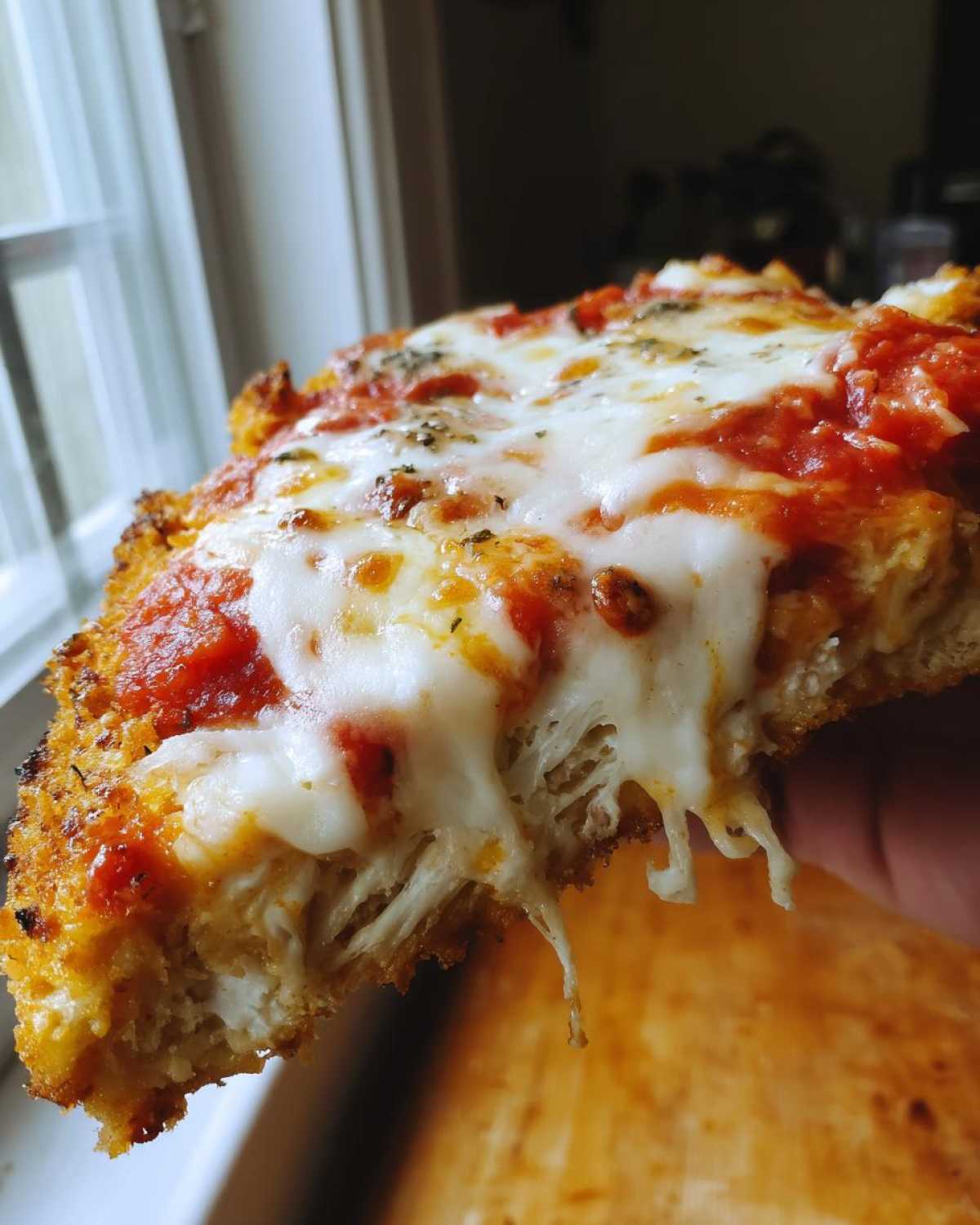 Close-up of a thick slice of Chicken Parmesan showing melted, stringy mozzarella cheese pulling away from the breaded chicken and marinara sauce.