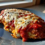 A close-up of a freshly baked Chicken Parmesan cutlet covered in rich tomato sauce and melted mozzarella cheese.