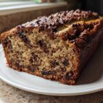 A close-up of a freshly baked slice of Chocolate Chip Banana Bread on a white plate.