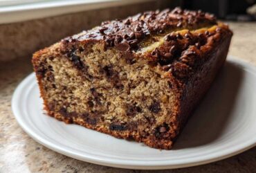 A close-up of a freshly baked slice of Chocolate Chip Banana Bread on a white plate.